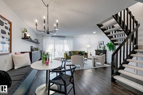 Open-concept living area featuring dark wood-finish flooring, a built-in banquette, and a contemporary chandelier - 19F Meadowlark Village Nw, Edmonton, AB - Indoor