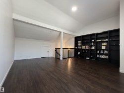 Spacious loft area featuring dark wood-finish flooring, a built-in black bookcase, and a vaulted ceiling with recessed lighting - 
