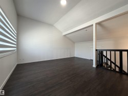 Spacious room featuring vaulted ceilings, dark wood-finish flooring, a contemporary window blind, recessed lighting, and a black open-spindle stair railing - 