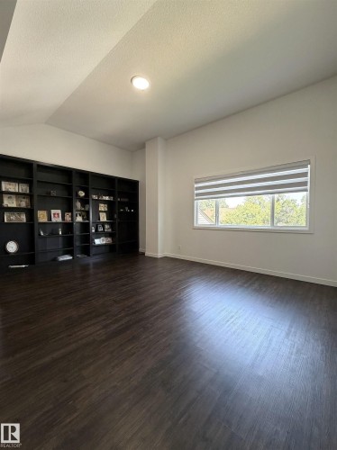 Spacious room featuring dark wood-finish flooring, a large window with dual blinds, recessed lighting, and extensive built-in shelving - 19F Meadowlark Village Nw, Edmonton, AB - Indoor