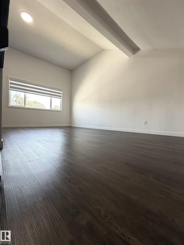 Expansive room featuring dark wood-finish flooring, vaulted ceilings with exposed beams, recessed lighting, and a horizontal window with adjustable blinds - 19F Meadowlark Village Nw, Edmonton, AB - Indoor Photo Showing Other Room