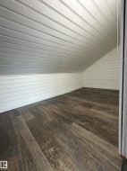Attic space featuring wood-finish flooring, white beadboard walls, and a sloped beadboard ceiling - 