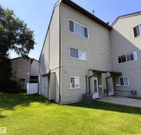 Rear exterior featuring light grey siding, multiple windows, a ground-level patio, and a grassy yard - 