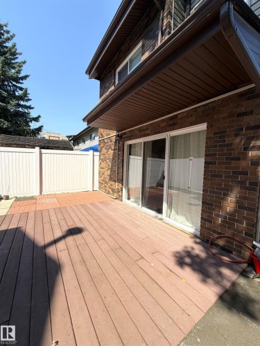 Spacious wood-finish deck with brick exterior, sliding glass doors, white privacy fencing, and an overhead soffit - 19F Meadowlark Village Nw, Edmonton, AB - Outdoor With Deck Patio Veranda With Exterior