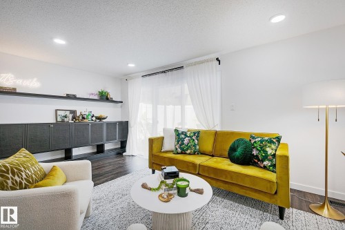 Spacious living area featuring dark wood-finish flooring, recessed lighting, and a full wall of built-in cabinetry with integrated shelving - 19F Meadowlark Village Nw, Edmonton, AB - Indoor Photo Showing Living Room