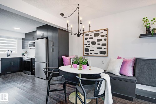 Open-concept kitchen and dining area featuring dark wood-finish flooring, a contemporary black chandelier, a built-in banquette, sleek black cabinetry, and stainless steel appliances - 19F Meadowlark Village Nw, Edmonton, AB - Indoor