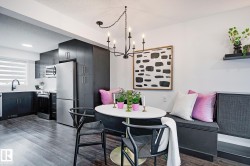 Open-concept kitchen and dining area featuring dark wood-finish flooring, a contemporary black chandelier, a built-in banquette, sleek black cabinetry, and stainless steel appliances - 