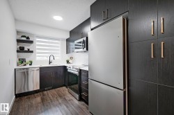 Contemporary kitchen featuring dark wood-finish cabinetry with gold-tone hardware, stainless steel appliances, wood-finish flooring, and a white tile backsplash - 