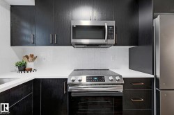 Modern kitchen featuring black cabinetry with sleek hardware, white countertops, and a white subway tile backsplash - 