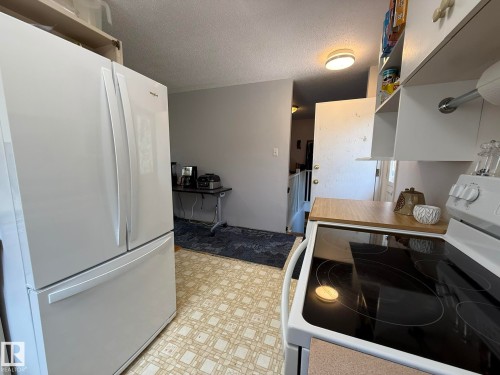 Kitchen featuring a white French-door refrigerator, a white electric range with a black smooth cooktop, and a wood-finish countertop - 10837 155 Street Nw, Edmonton, AB - Indoor