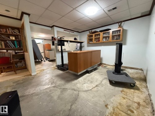 Basement area featuring a drop ceiling with recessed lighting, exposed concrete flooring, and built-in shelving - 10837 155 Street Nw, Edmonton, AB - Indoor