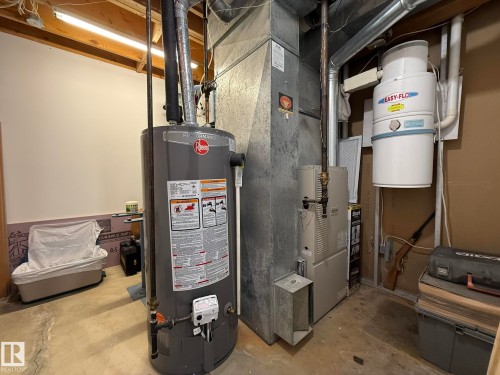 Utility area featuring a water heater, furnace, and central vacuum system, set against a painted wall and exposed ceiling joists - 10837 155 Street Nw, Edmonton, AB - Indoor Photo Showing Basement