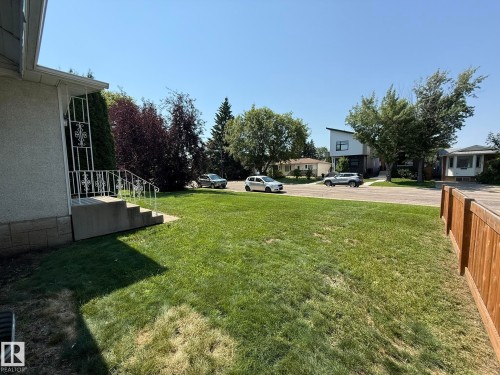 Expansive front lawn with mature greenery and a concrete porch featuring decorative metal railings - 10837 155 Street Nw, Edmonton, AB - Outdoor