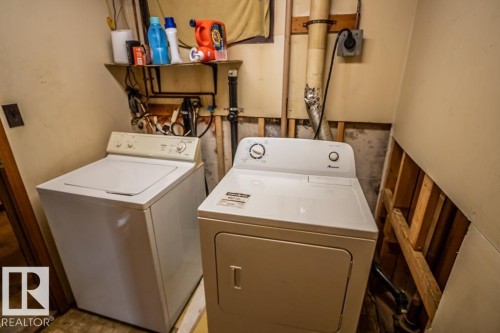 Laundry area featuring a top-load washing machine, front-load dryer, and wall-mounted shelving - 5009 47 Ave, St. Paul Town, AB - Indoor Photo Showing Laundry Room
