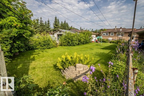 Expansive rear yard featuring a manicured lawn, established perimeter shrubbery, a wood-sided shed, a decorative stone-block planter, and various flowering plants - 5009 47 Ave, St. Paul Town, AB - Outdoor