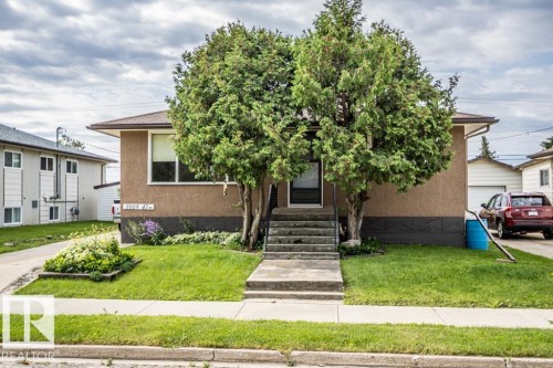 Stucco exterior with a dark trim foundation, mature front yard trees, concrete front steps, a dedicated driveway, and a single-car detached garage - 5009 47 Ave, St. Paul Town, AB - Outdoor