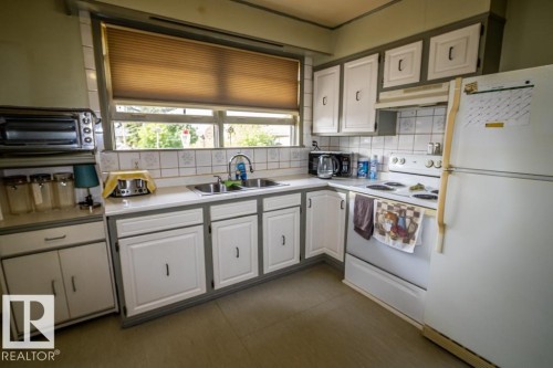 Functional kitchen space featuring white cabinetry with grey trim, a double basin sink, and white tile backsplash - 5009 47 Ave, St. Paul Town, AB - Indoor Photo Showing Kitchen With Double Sink