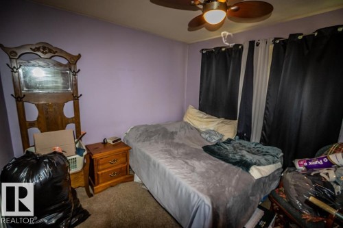 Carpeted room with a ceiling fan light fixture, natural wood-finish nightstand, and window with dark drapes - 5009 47 Ave, St. Paul Town, AB - Indoor Photo Showing Bedroom