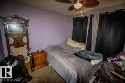 Carpeted room with a ceiling fan light fixture, natural wood-finish nightstand, and window with dark drapes - 