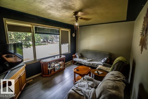 Large window array with privacy blinds, dark wood-finish flooring, recessed ceiling with perimeter trim, and a ceiling fan with integrated lighting - 5009 47 Ave, St. Paul Town, AB - Indoor Photo Showing Other Room