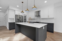 Kitchen featuring a large island with white countertop, stainless steel appliances, herringbone wood-finish flooring, and pendant lighting - 