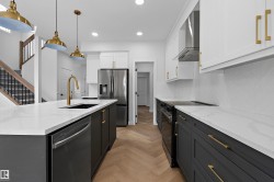 Contemporary kitchen featuring a galley layout with dual islands, white cabinetry with brushed brass hardware, white subway tile backsplash, white quartz countertops, stainless steel appliances, brass pendant lighting, and wood-finish flooring throughout - 