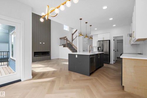 Open-concept living space showcasing herringbone wood-finish flooring, a central kitchen island with black cabinetry, stainless steel appliances, white quartz countertops, and pendant lighting - 1737 Crossbill Loop Nw, Edmonton, AB - Indoor Photo Showing Kitchen With Upgraded Kitchen