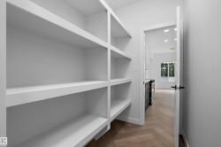 Spacious walk-in closet featuring built-in shelving with white painted finishes and wood-finish flooring - 