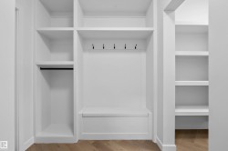 Spacious walk-in closet featuring custom white cabinetry with multiple shelving units, a center island with drawer storage, a clothing rod, and integrated hooks for organized accessory storage - 