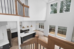 Two-story living area with high ceilings, multiple large windows, wood-finish flooring, and a contemporary kitchen featuring a large island with a sink and pendant lighting - 