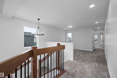 Staircase featuring wood-finish handrail with black iron balusters, recessed lighting, and a modern chandelier - 1737 Crossbill Loop Nw, Edmonton, AB - Indoor Photo Showing Other Room