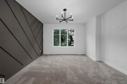 Textured accent wall, neutral carpeting, white trim, recessed window, and a central chandelier - 