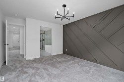 Carpeted room featuring a geometric accent wall and a modern chandelier - 