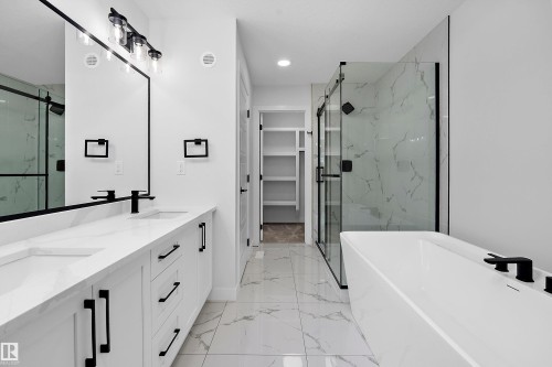 Dual vanity with integrated sinks, a freestanding tub, and a glass-enclosed shower with a black-framed door - 1737 Crossbill Loop Nw, Edmonton, AB - Indoor Photo Showing Bathroom