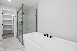 Freestanding soaking tub with matte black fixtures, glass-enclosed shower with marble-look tile surround, and an adjacent walk-in closet with built-in shelving - 