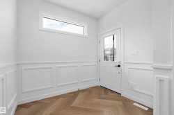 Entryway featuring wainscoting, wood-finish flooring in a herringbone pattern, a white door with glass panels, and a clerestory window - 