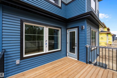 Modern blue exterior with composite deck featuring warm wood-tone decking, large dual-pane sliding glass doors, and contemporary black metal railing - 1737 Crossbill Loop Nw, Edmonton, AB - Outdoor With Deck Patio Veranda