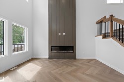 Vaulted ceiling, herringbone wood-finish flooring, electric fireplace, large windows, and a wood staircase with black iron spindles - 