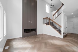 High ceilings with a prominent fireplace feature wall, light wood-finish herringbone flooring, and a staircase with wood handrails and black balusters - 
