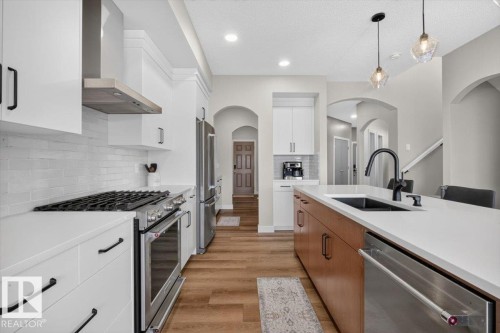 Modern kitchen featuring a gas range with a stainless steel hood, white cabinetry, and wood-finish flooring - 347 Bluff Cove, Leduc, AB - Indoor Photo Showing Kitchen With Upgraded Kitchen