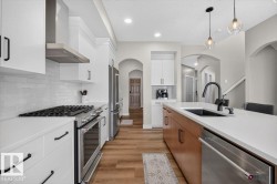 Modern kitchen featuring a gas range with a stainless steel hood, white cabinetry, and wood-finish flooring - 