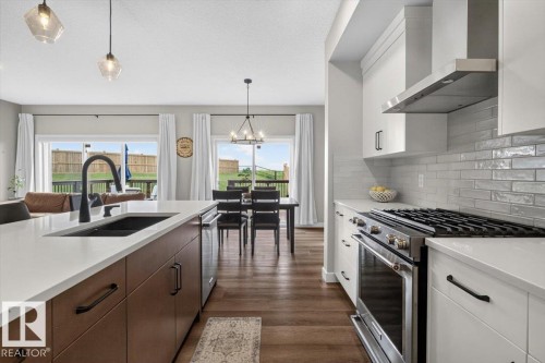 Modern kitchen featuring a large island with an undermount sink, white countertops, and wood-finish lower cabinetry - 347 Bluff Cove, Leduc, AB - Indoor Photo Showing Kitchen With Double Sink With Upgraded Kitchen