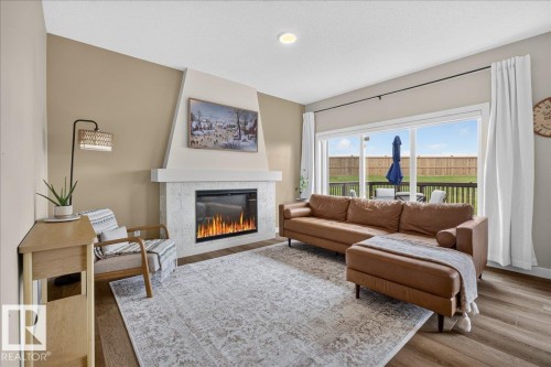 Living area featuring a textured accent wall, an electric fireplace with a white mantel, and wood-finish flooring - 347 Bluff Cove, Leduc, AB - Indoor Photo Showing Living Room With Fireplace