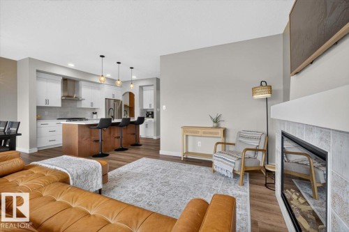 Open-concept living space featuring wood-finish flooring, a contemporary fireplace with a tiled surround, and a kitchen island with seating - 347 Bluff Cove, Leduc, AB - Indoor Photo Showing Living Room With Fireplace