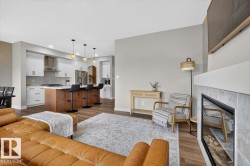 Open-concept living space featuring wood-finish flooring, a contemporary fireplace with a tiled surround, and a kitchen island with seating - 