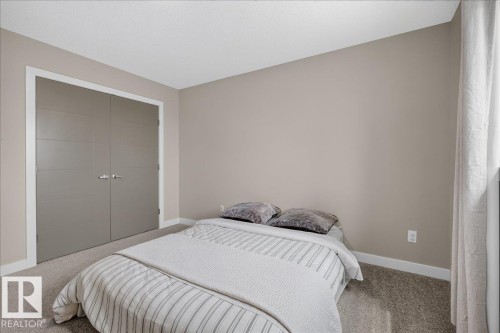 Spacious bedroom featuring neutral wall paint, light-toned carpet flooring, white baseboards, and a pair of gray bi-fold closet doors with chrome hardware - 347 Bluff Cove, Leduc, AB - Indoor Photo Showing Bedroom