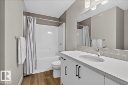 Bathroom featuring a white vanity with integrated sink, coordinating white bathtub and shower surround, subway tile accent, wood-finish flooring, and a large mirror with overhead lighting - 