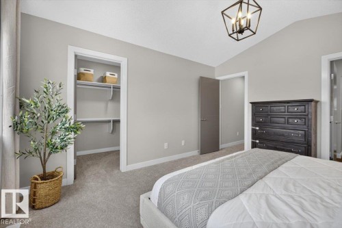 Spacious room featuring vaulted ceilings, light gray walls, plush carpeting, and a modern geometric ceiling light fixture - 347 Bluff Cove, Leduc, AB - Indoor Photo Showing Bedroom