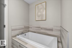 Built-in soaking tub with chrome fixtures, surrounded by large format porcelain tile with a natural wood-grain finish - 