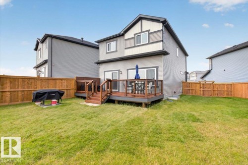 Spacious backyard featuring a two-story residence with a multi-tone exterior, a wood deck with dark railings, and a full perimeter wood fence - 347 Bluff Cove, Leduc, AB - Outdoor With Deck Patio Veranda With Exterior